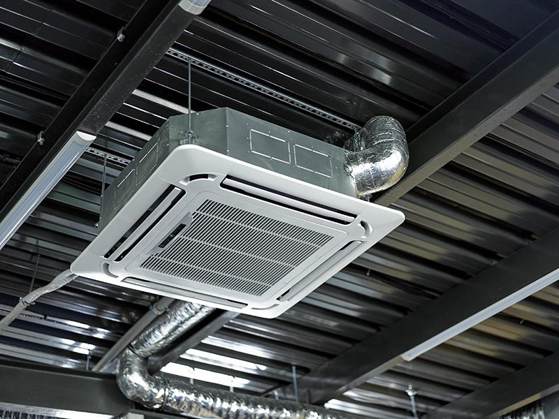 Een cassette-airco in het plafond van een bedrijfsruimte, met de luchtkanalen erachter zichtbaar.